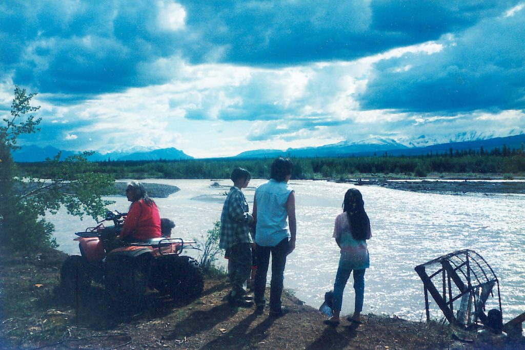 Four people standing by river. 