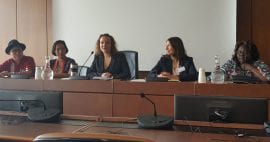 Photo of five people sitting at the front of a room presenting.