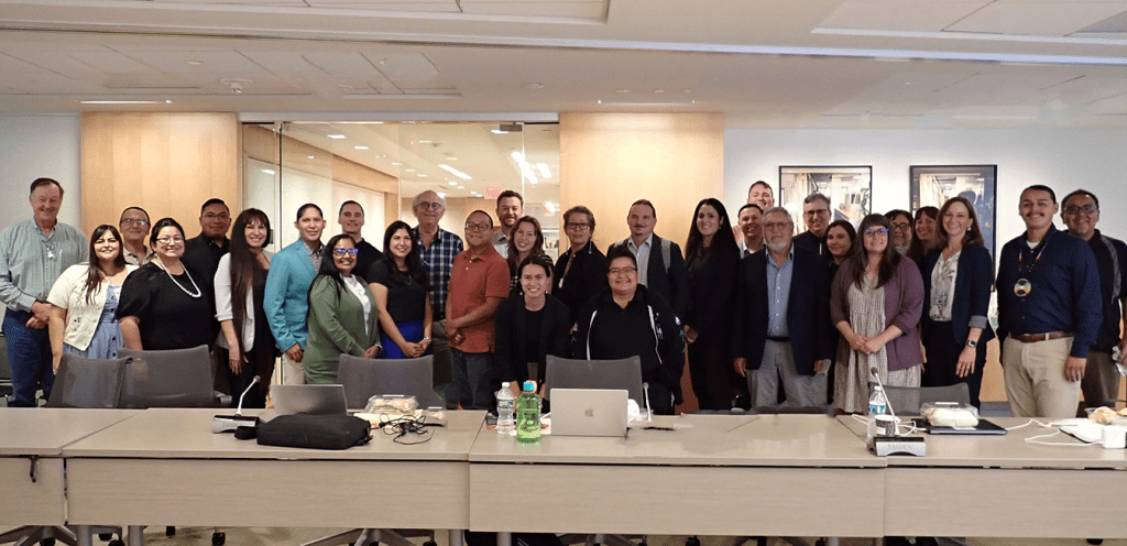 A large group of people (many of them Native American) standing in an office, smiling at the camera.