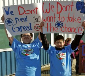 Photo of two people holding handmade signs that say anti-Pebble Mine slogans. 