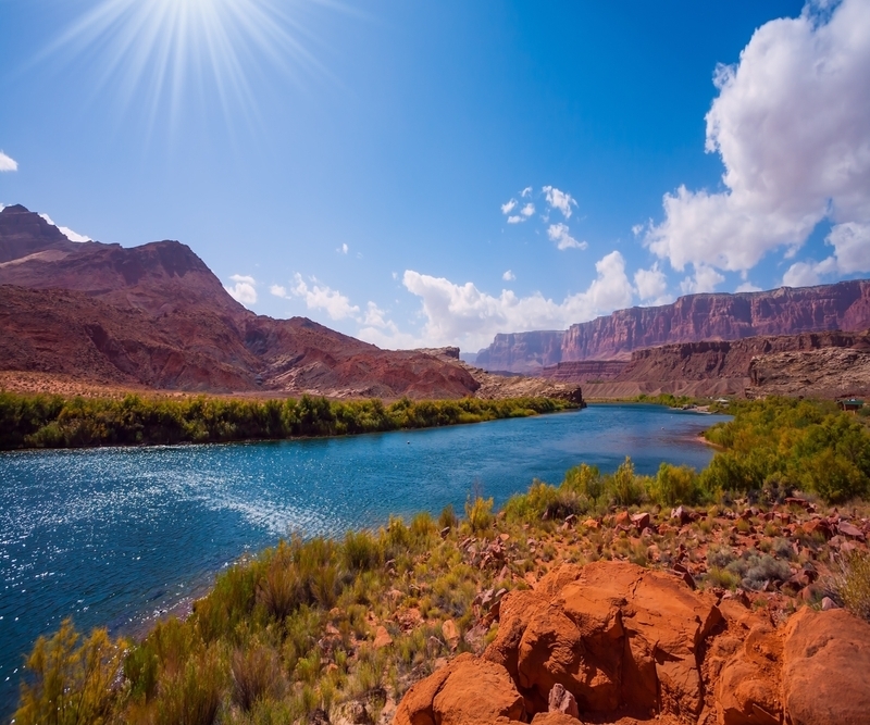 Photo of red cliffs in the distance with bright blue river curving towards the viewer. 