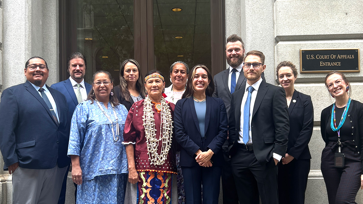 A group of ten people standing and smiling in front of a stone court house. 