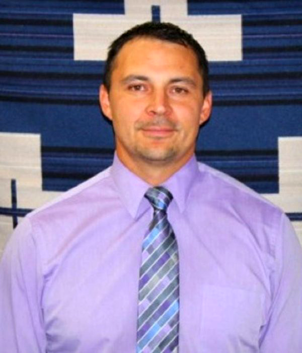 Photo of man with dark hair wearing a tie and smiling at the camera.